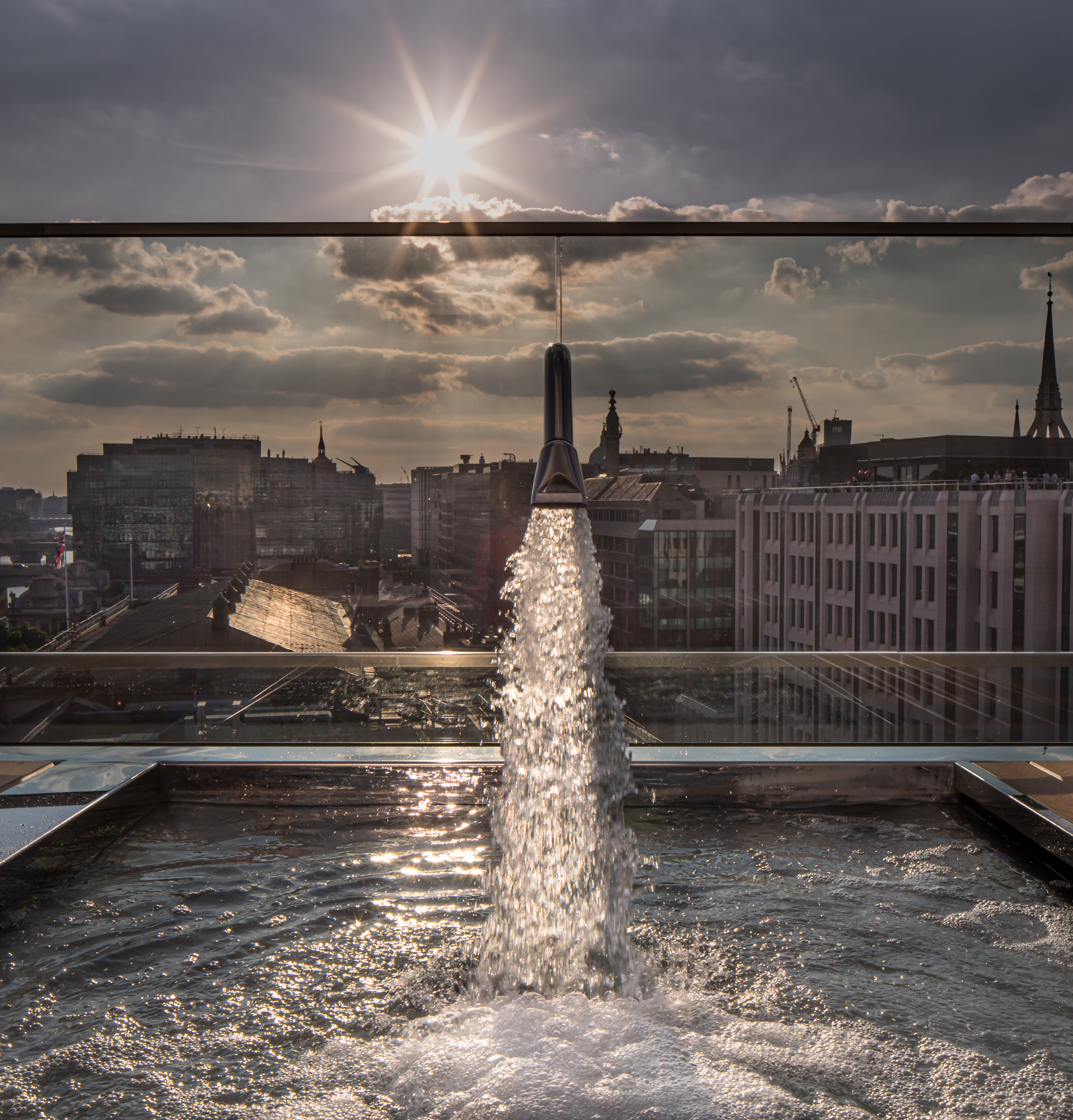 Large Spa Jet with water gushing out of the funnel.  The sunn is shining on the water as it enters the Spa sparkling from the sun setting in the distance.  The roof top spa has far reaching views of London Architecture and buildings that sit on the banks of the Thames, London - Architectural Photography by Di Jones Photography